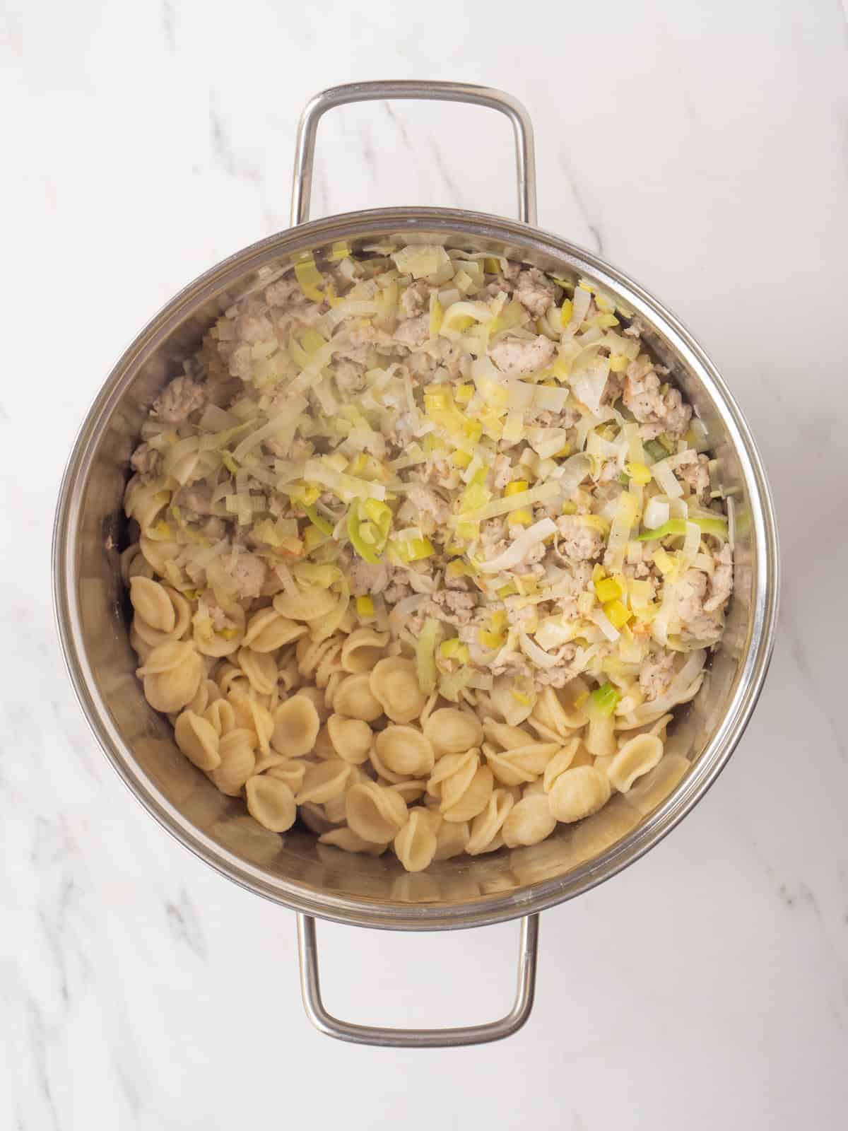 A pot with the leeks and sausage mixture tossed with orecchiette pasta, along with pasta water added to thicken the sauce.