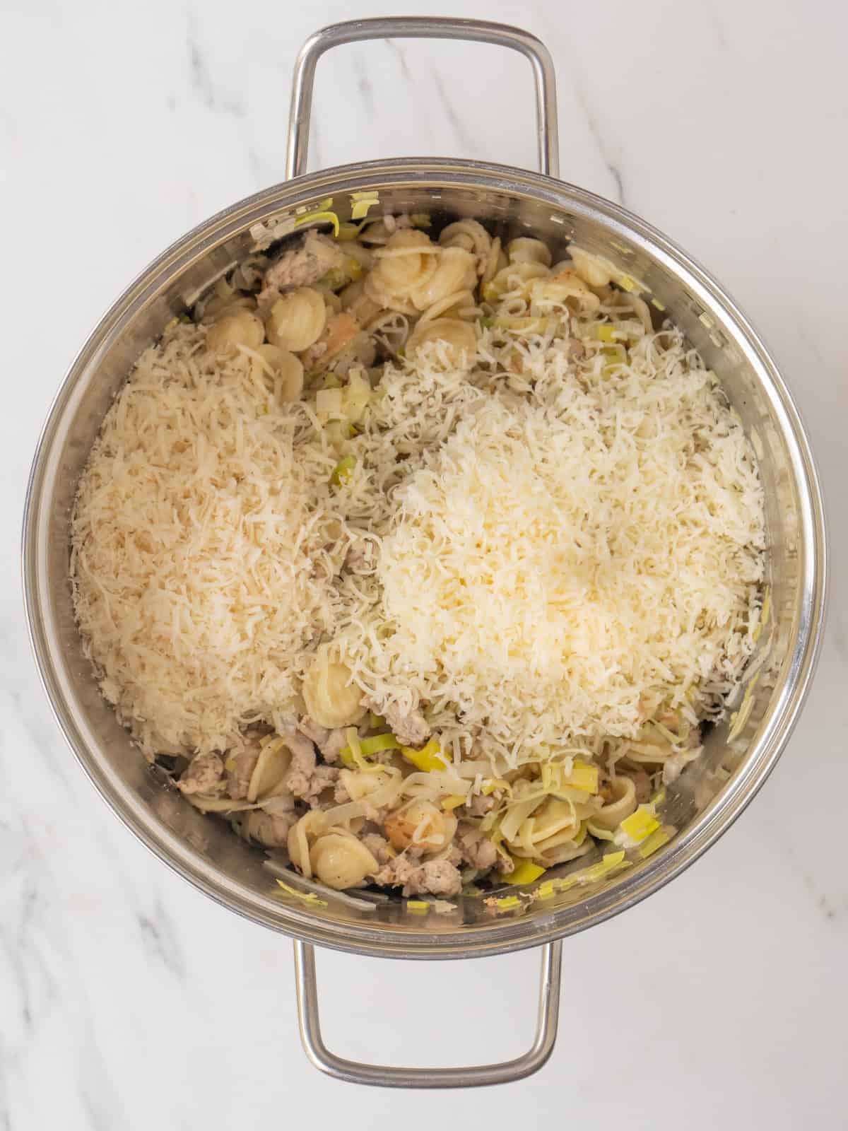 A pot with sausage and leeks pasta along with shredded asiago and parmesan added.