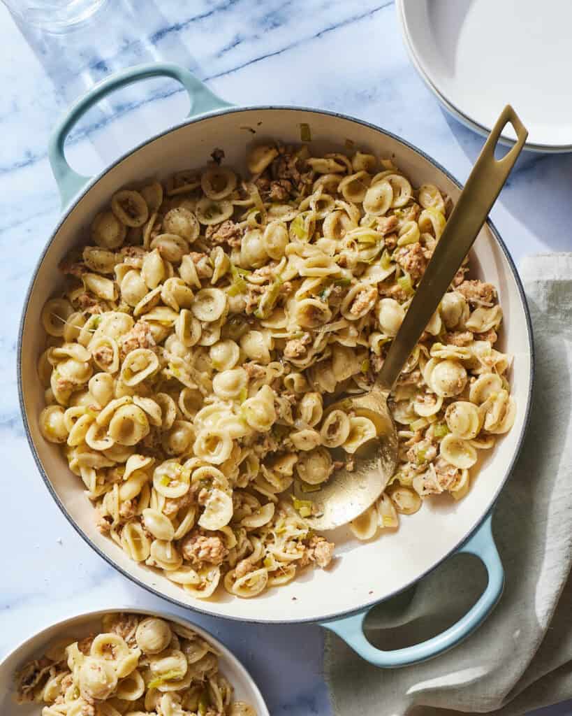 A braiser with sausage and leek orecchiette with some served into a bowl on the side.