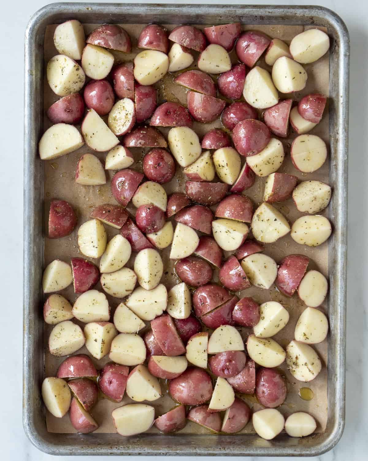 Quartered potatoes on a baking sheet drizzled with olive oil salt and pepper.  