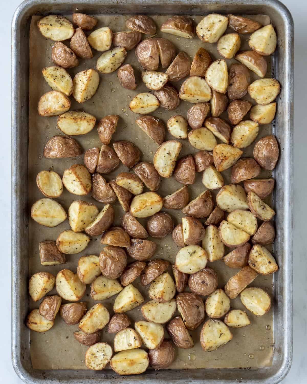 Quartered potatoes that have been cooked sitting on a baking sheet with parchment paper.  