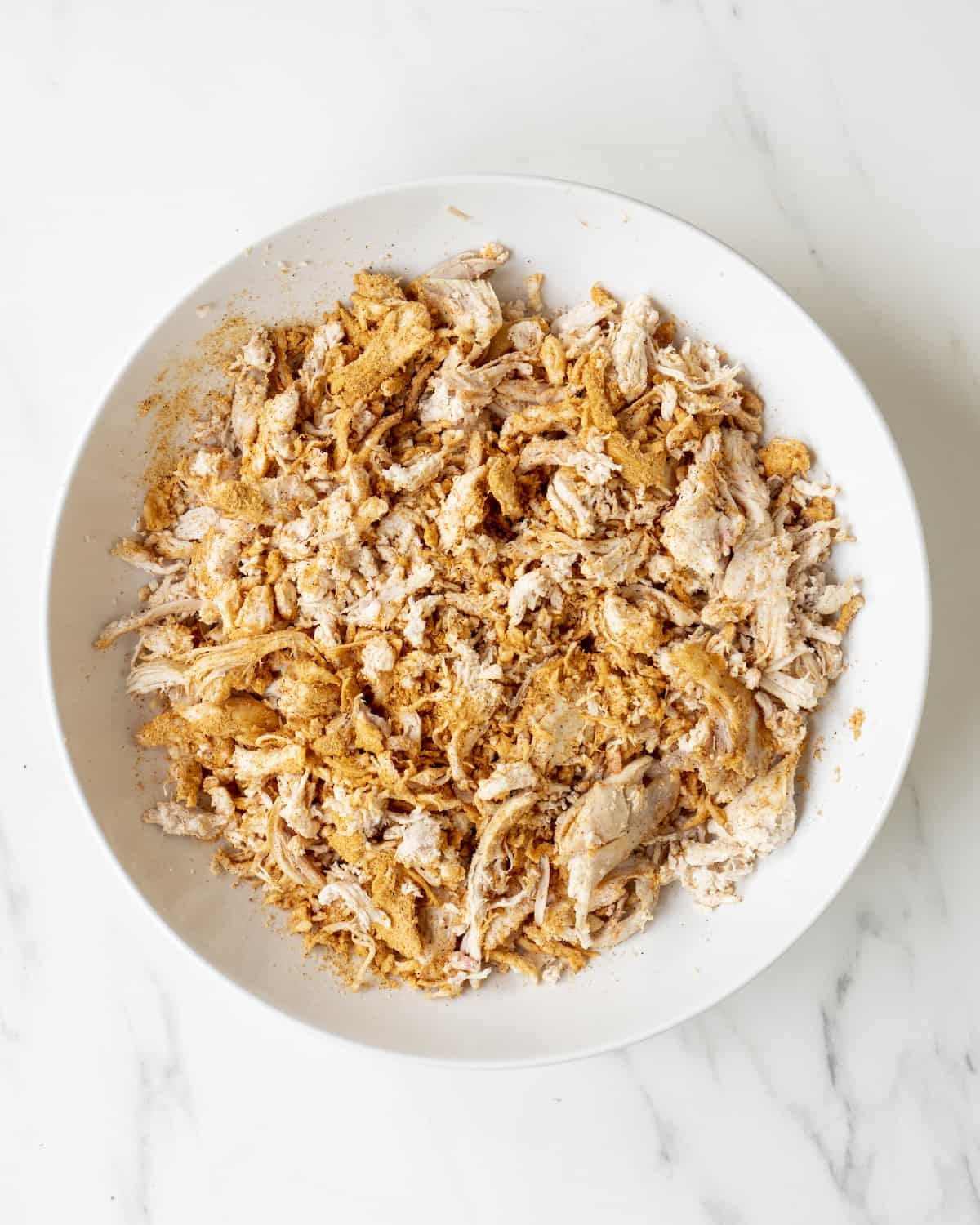 A white mixing bowl with shredded chicken tossed in taco seasoning.