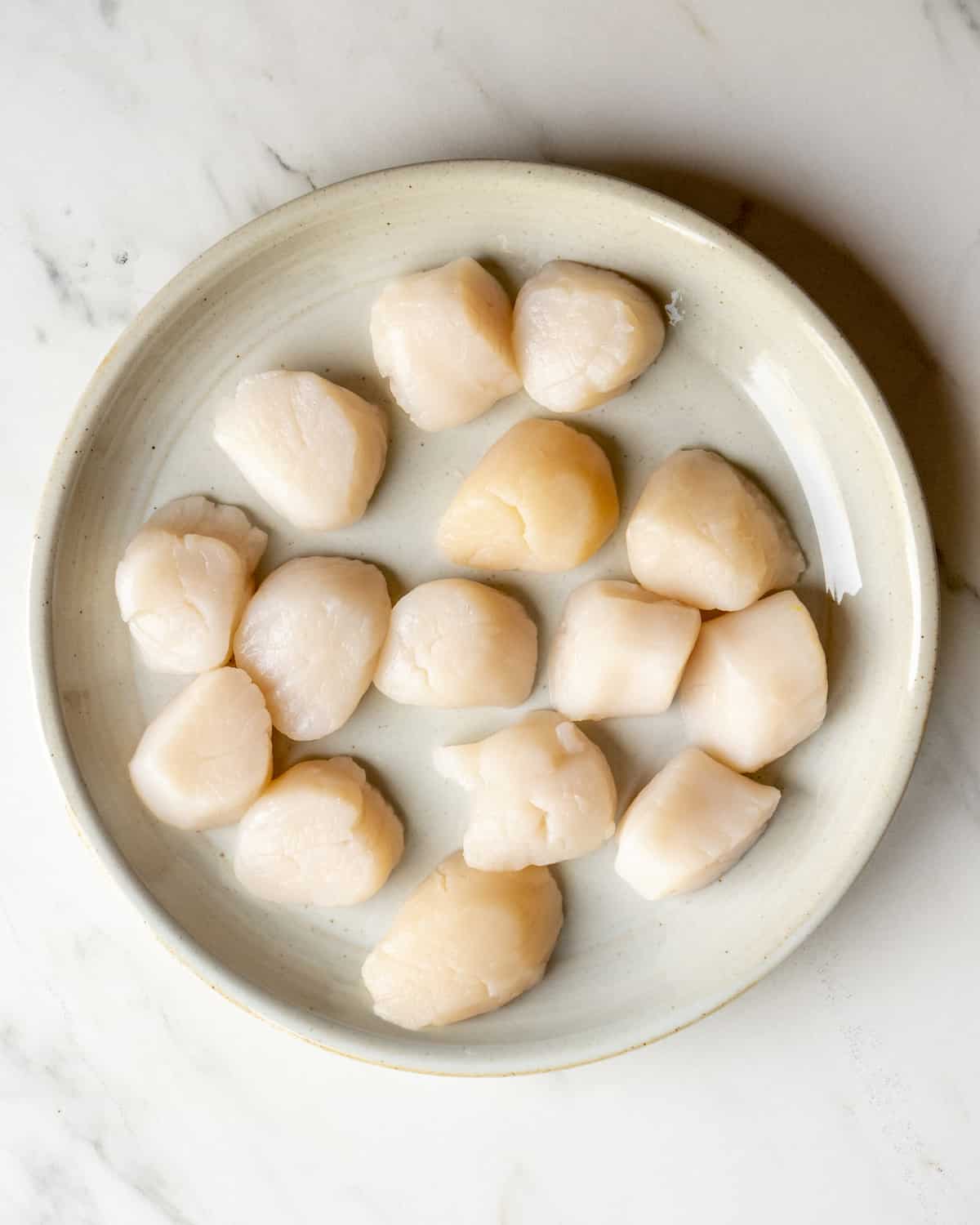 A plate of 14 scallops with the muscle removed and that have been patted dry with a paper towel.