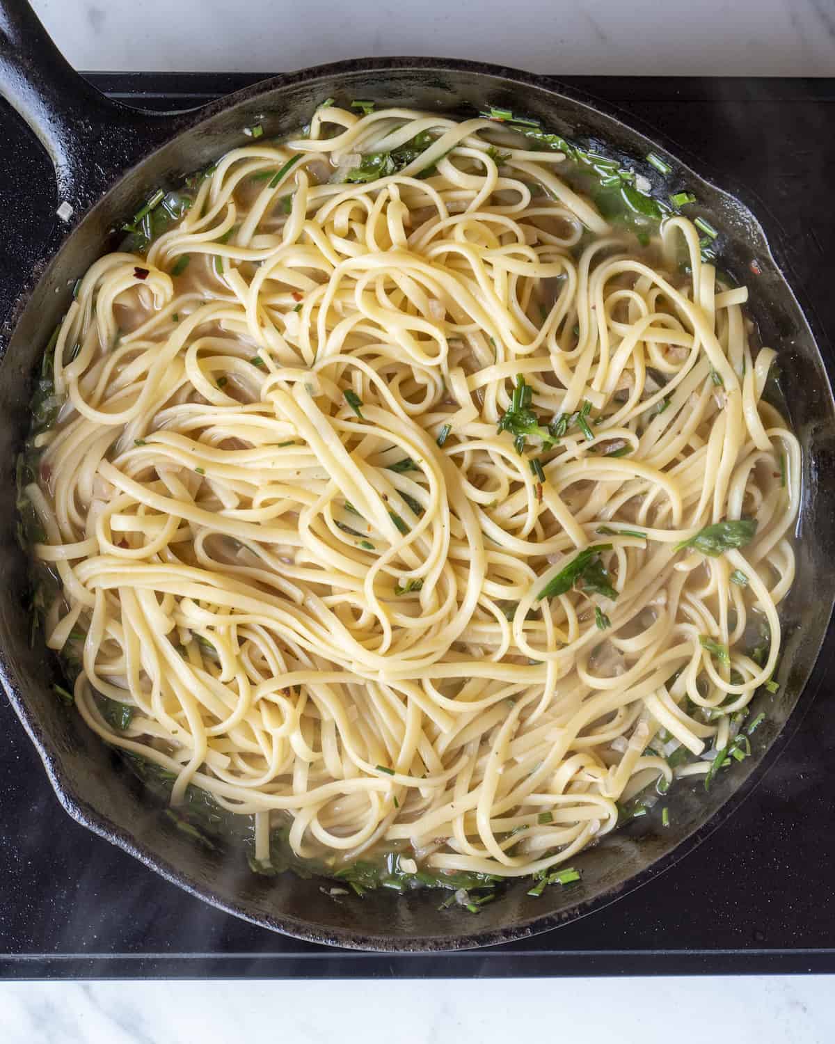 cooked linguine nestled in a cast iron skillet with a white wine lemon basil garlic sauce