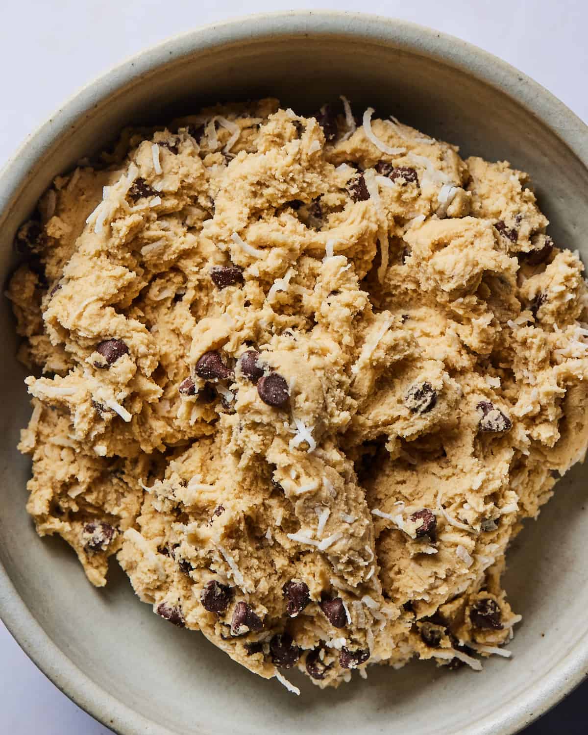 A close-up of a round ceramic bowl with Coconut Chocolate Chip Cookie dough.