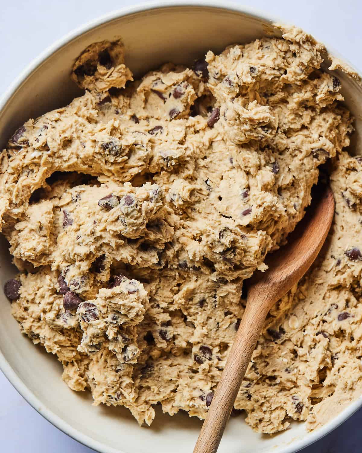 A bowl full of oatmeal chocolate chip cookie dough with a wooden spatula.