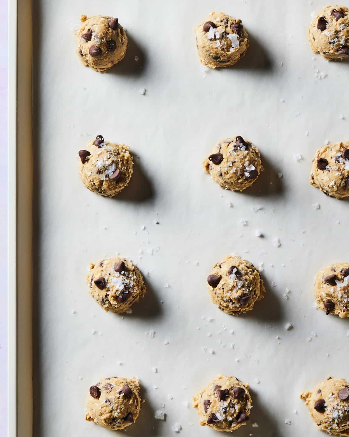 A parchment lined baking sheet with cookie dough scooped on to the sheet in a grid topped with flaky salt.