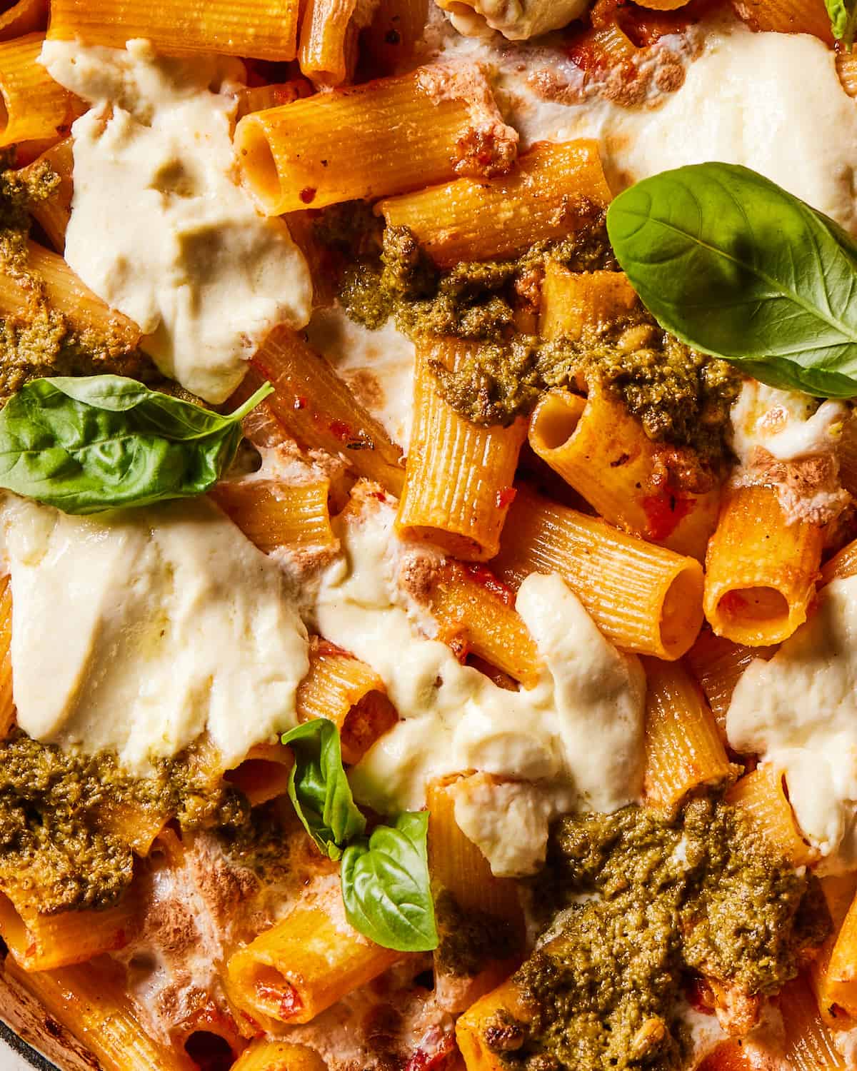 A closeup shot of baked rigatoni with ground chicken sausage, pesto and ricotta garnished with basil leaves.