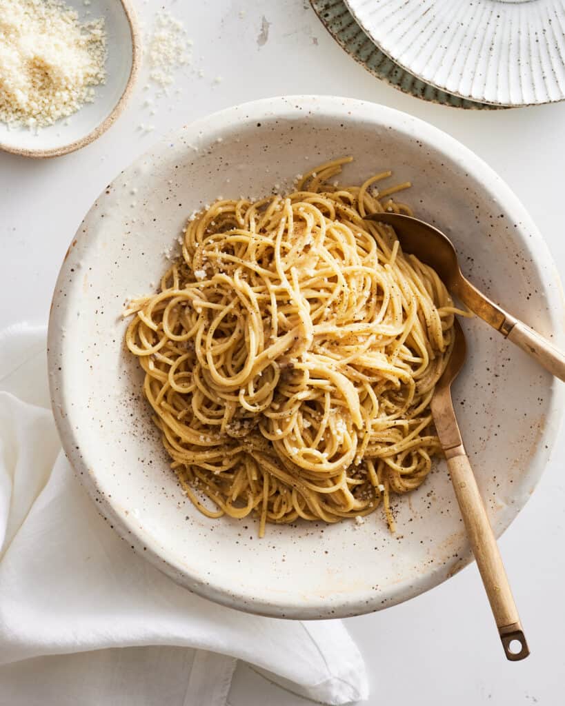 Cacio e Pepe in a speckled bowl sitting next to a bow of parmesan.  