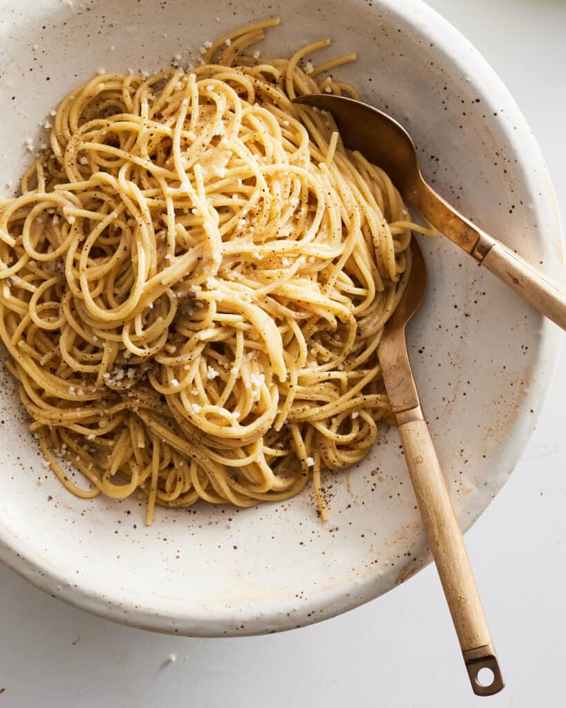 A speckled bowl of  Cacio e Pepe with a fork and a spoon.  