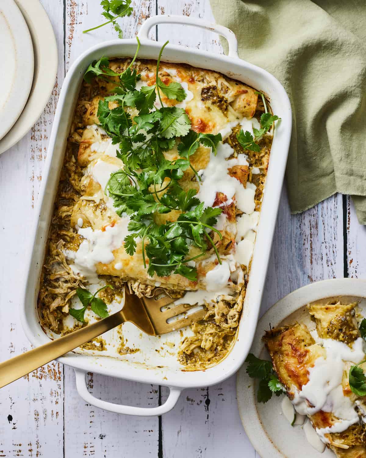 Green Chicken Enchiladas in a casserole dish with cilantro leaves spread across the top of the dish.  