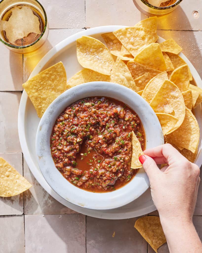 A bowl of salsa sitting on a plate with some tortilla chips.  