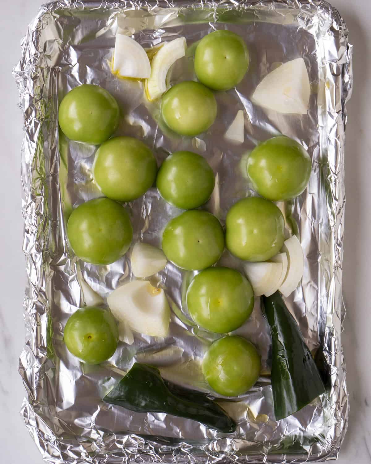 A baking sheet lined in tin foil with the poblanos, onions, and tomatillos.  