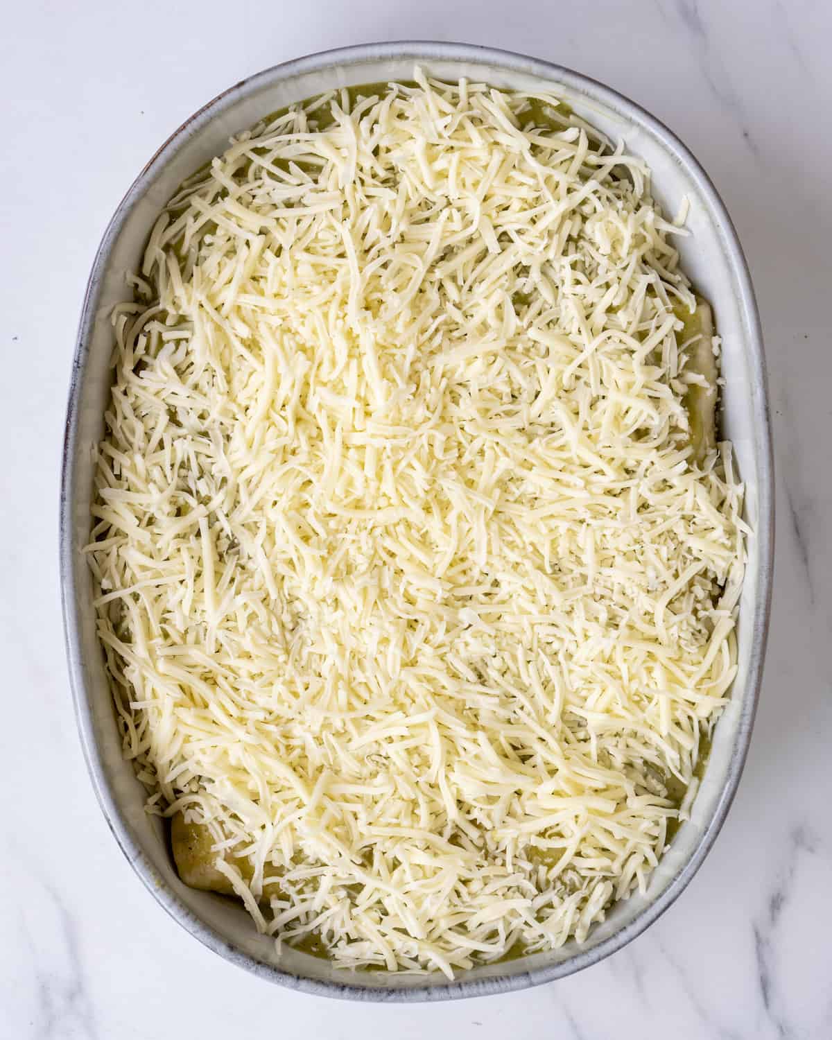 A baking dish full of enchiladas covered with shredded cheese.  