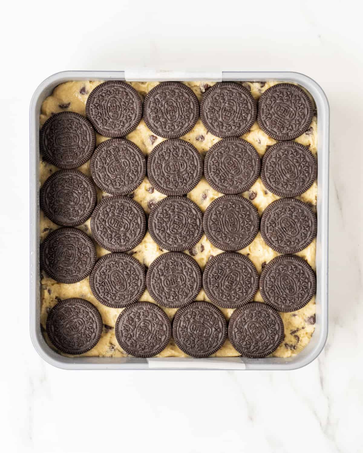 A baking pan filled with cookie dough and a layer of oreos.  