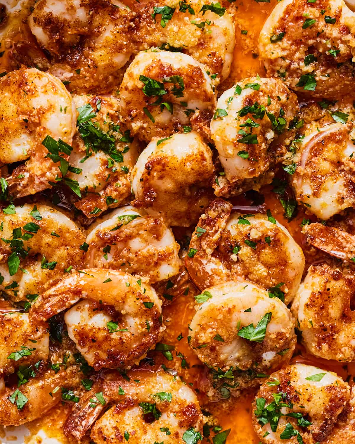 A tight overhead shot of cooked Hawaiian garlic shrimp in a chili garlic butter sauce with a garnish of minced parsley 
