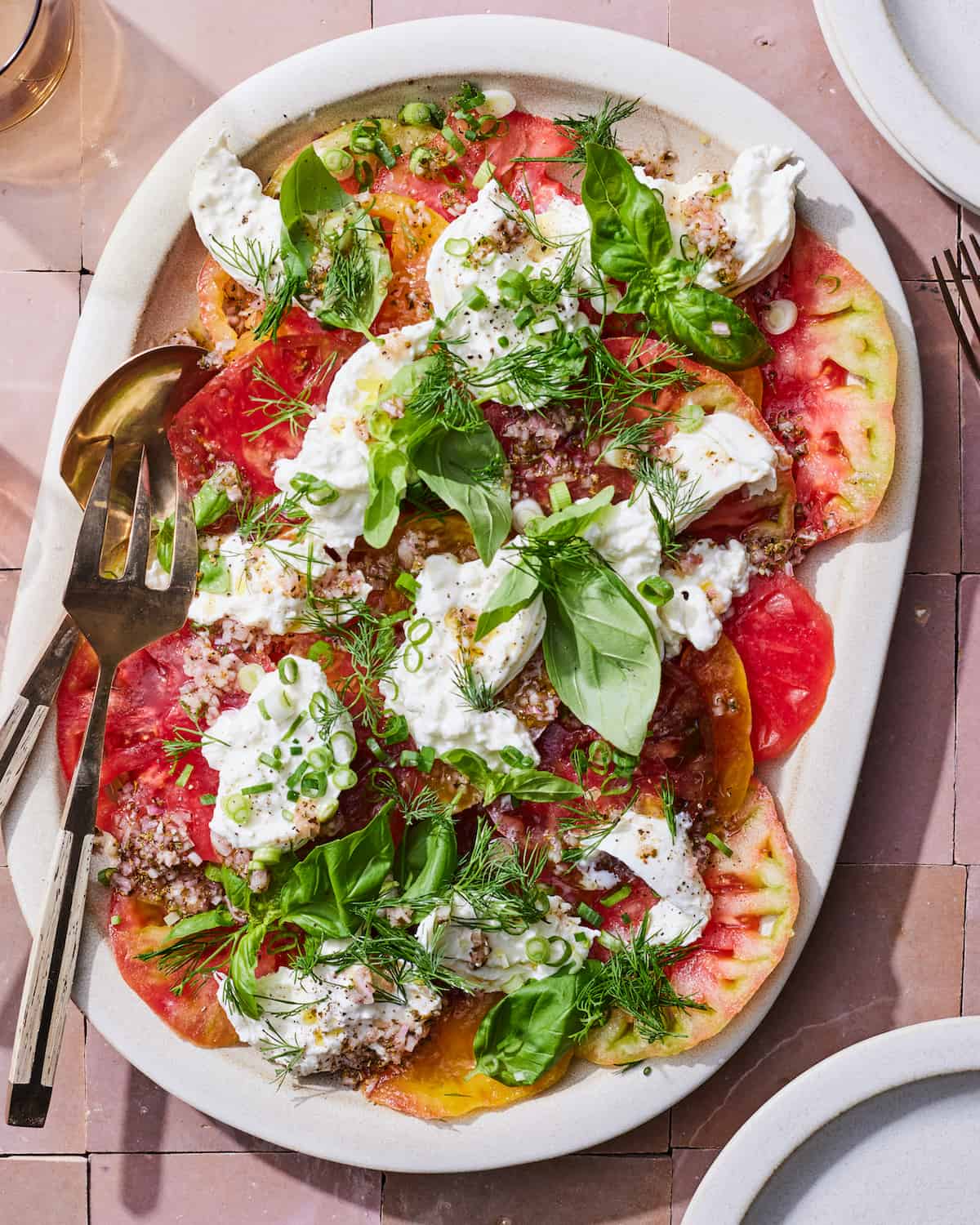 A serving platter with Heirloom tomatoes, burrata, fresh herbs, and oregano.  