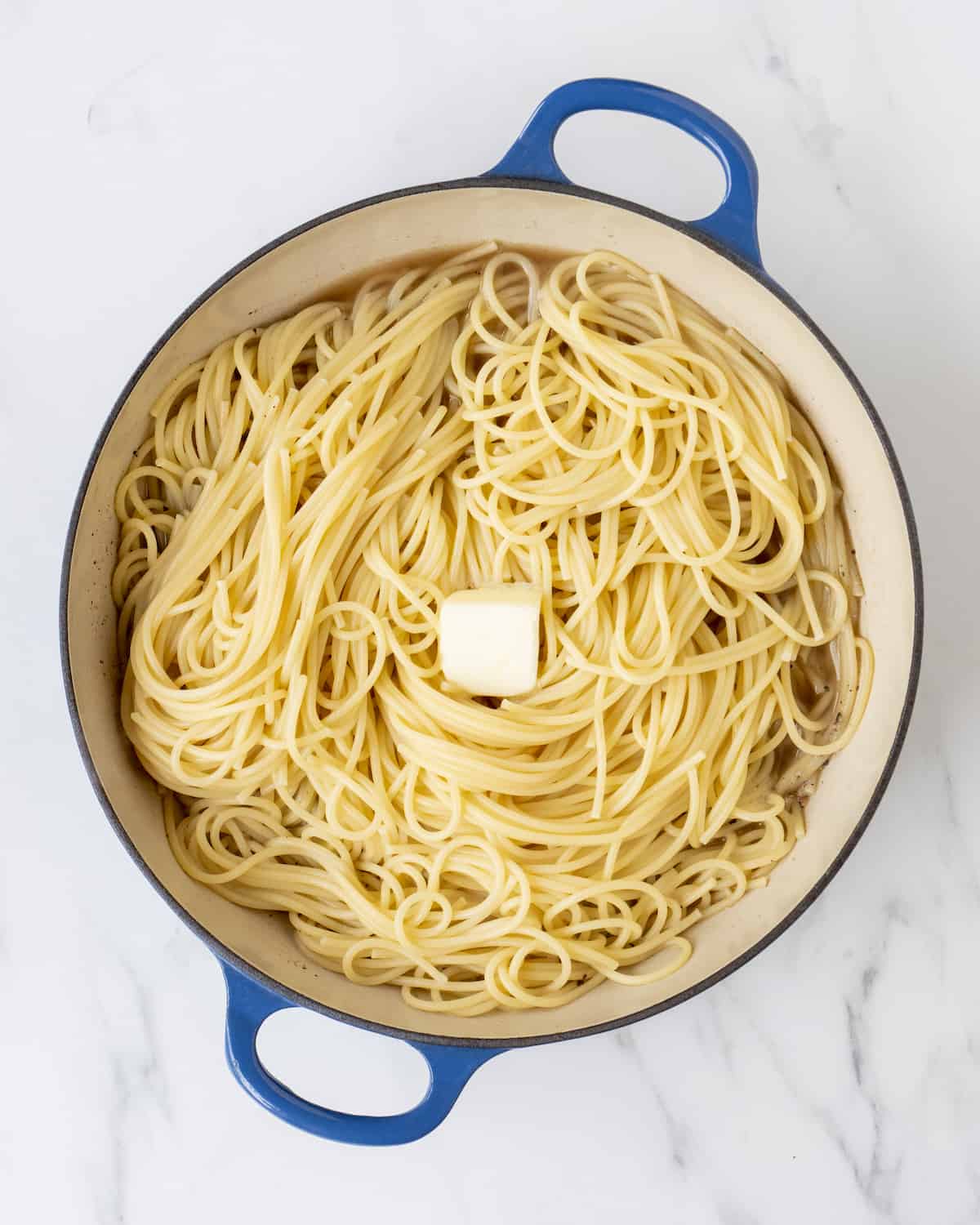 A large skillet with cooked spaghetti and a chunk of unmelted butter.  