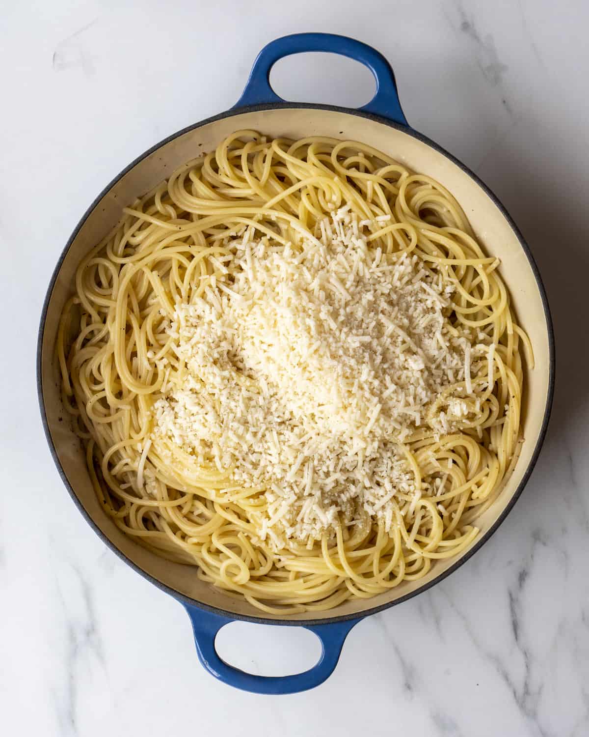 A large skillet with cooked spaghetti and shaved parmesan.  