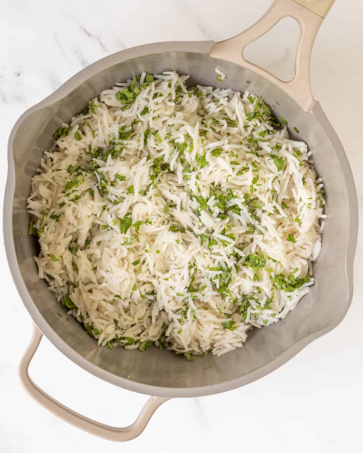 Fluffy cooked white rice with chopped cilantro in a saucepan.