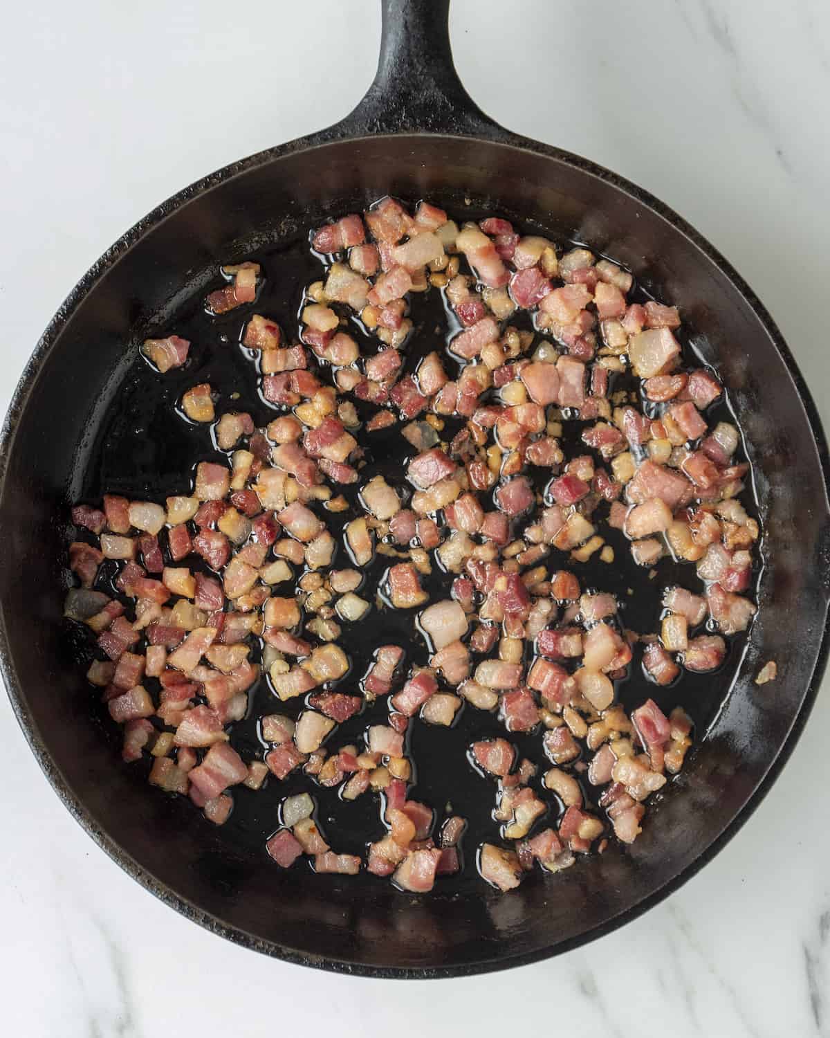 Diced pancetta frying in a cast iron skillet.