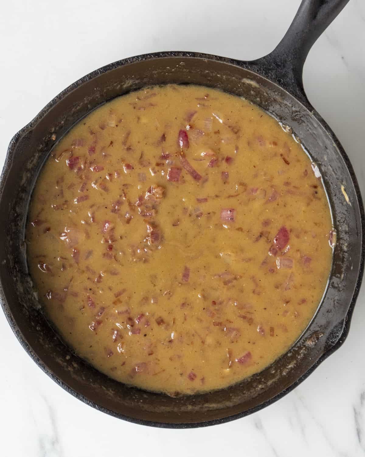 A warm potato salad dressing made of olive oil, champagne vinegar, red onion, and dijon mustard in a cast iron skillet.