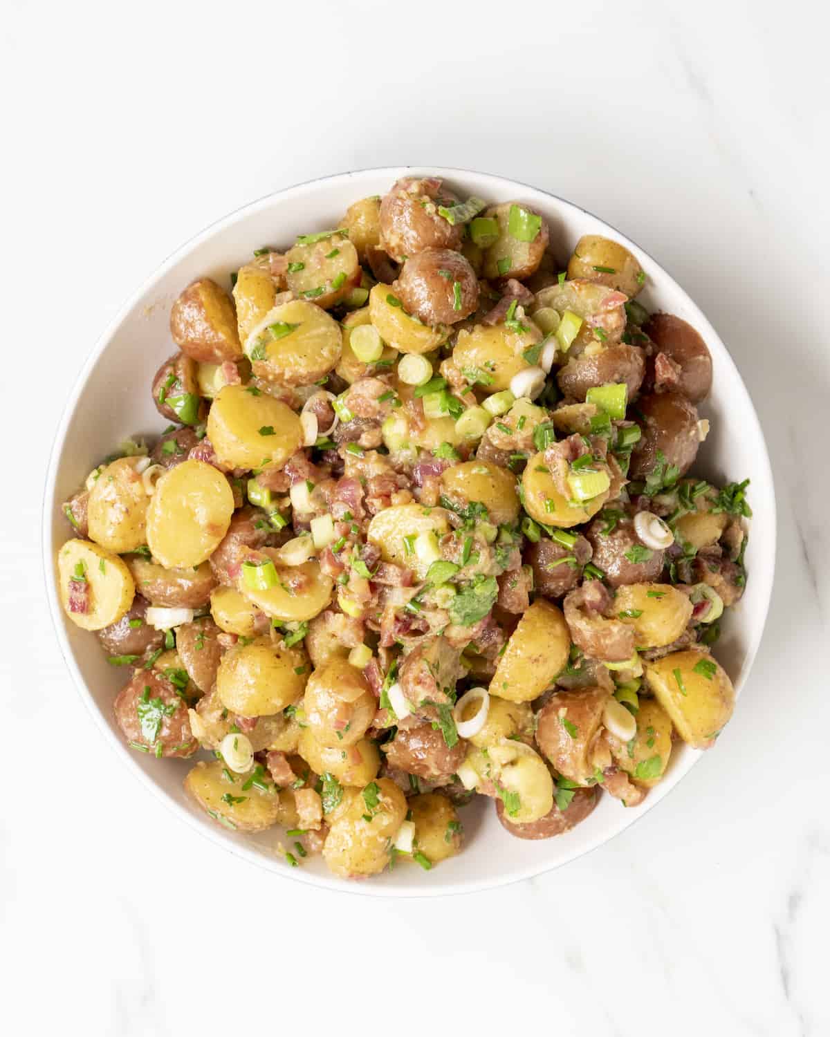 A large bowl of German potato salad with crispy diced pancetta, thinly sliced scallions, thinly sliced chives, and chopped parsley