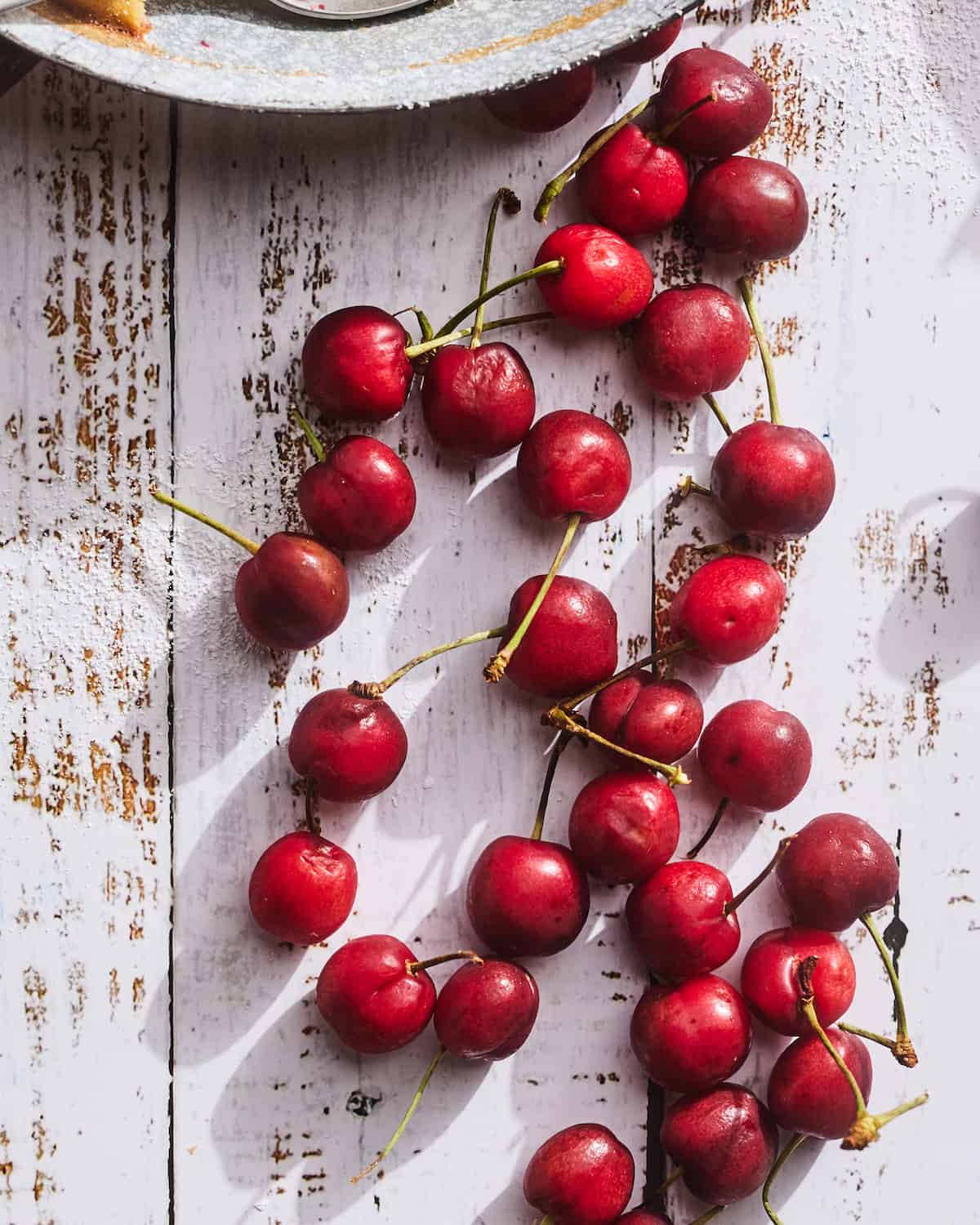 Whole red cherries with stems scattered on a white washed wooden table