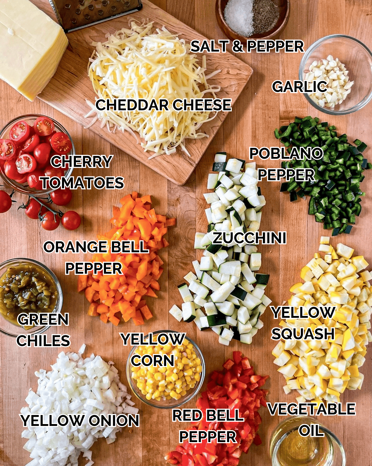 Calabacitas Ingredients prepped on a wooden cutting board.  Ingredients include cheddar cheese, salt and pepper, cherry tomatoes, garlic, poblano peppers, zucchini, orange bell peppers, green chiles, yellow corn, yellow squash, yellow onion, red bell pepper, and vegetable oil.  