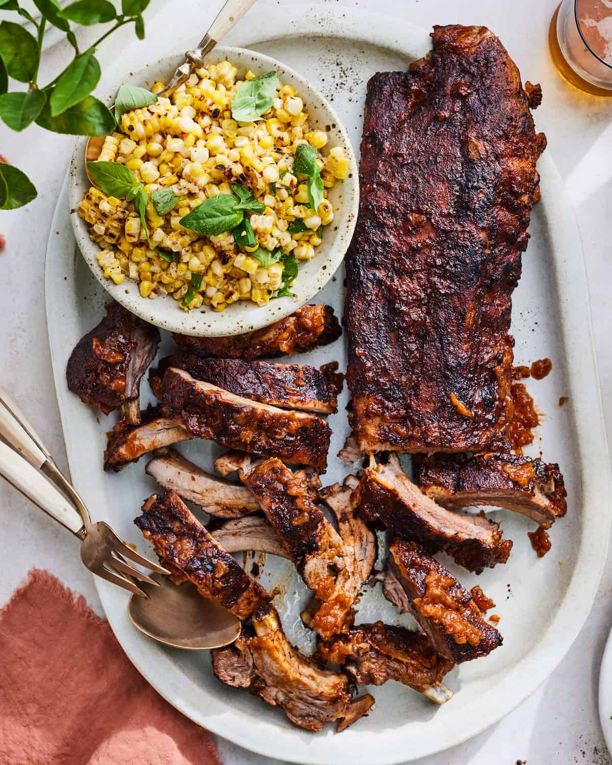 A platter of BBQ Baby Back Ribs with homemade BBQ sauce and a corn salad on the side. 