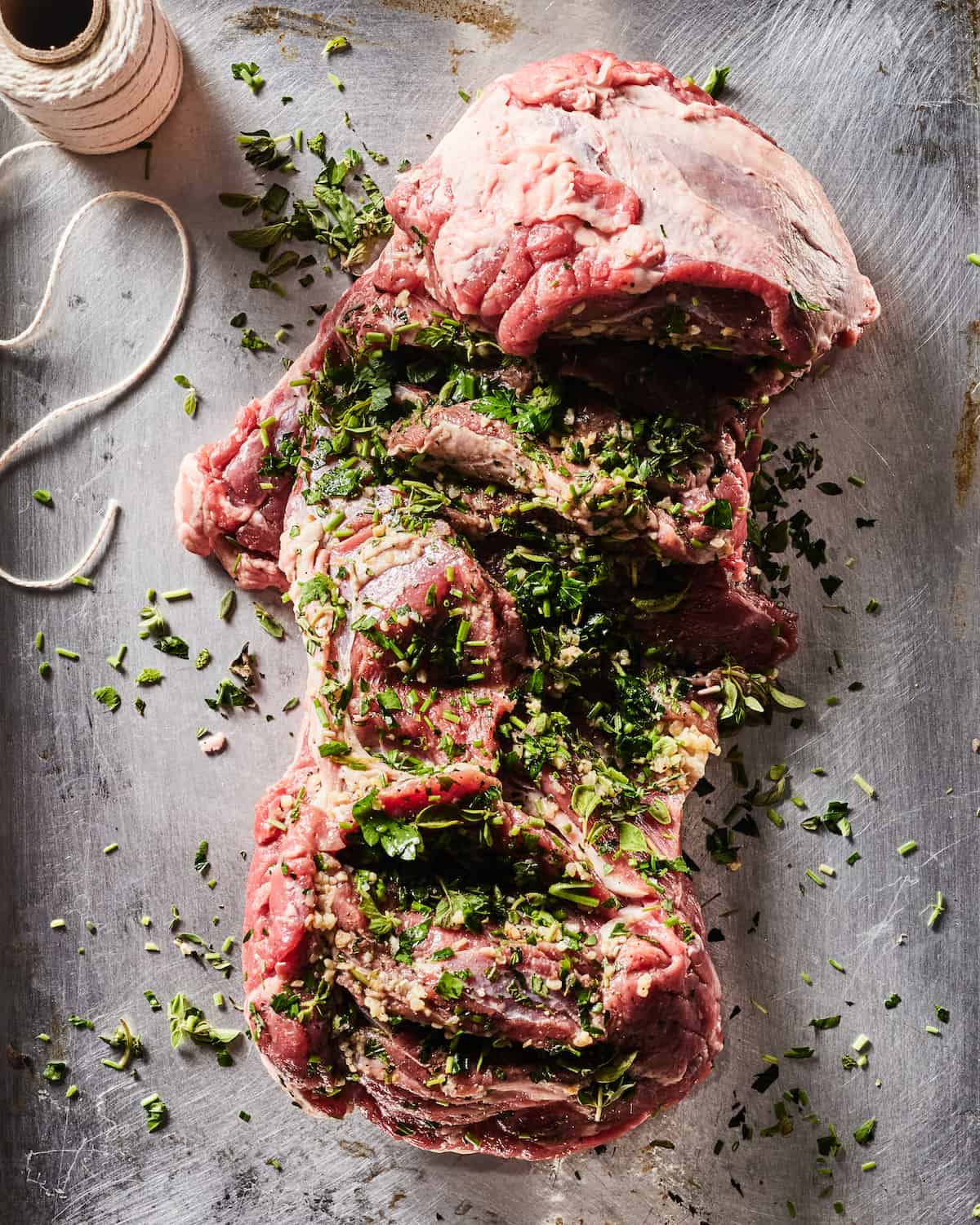 A leg of lamb laying flat on the counter. Sprinkled generously with salt and pepper garlic and herbs.  