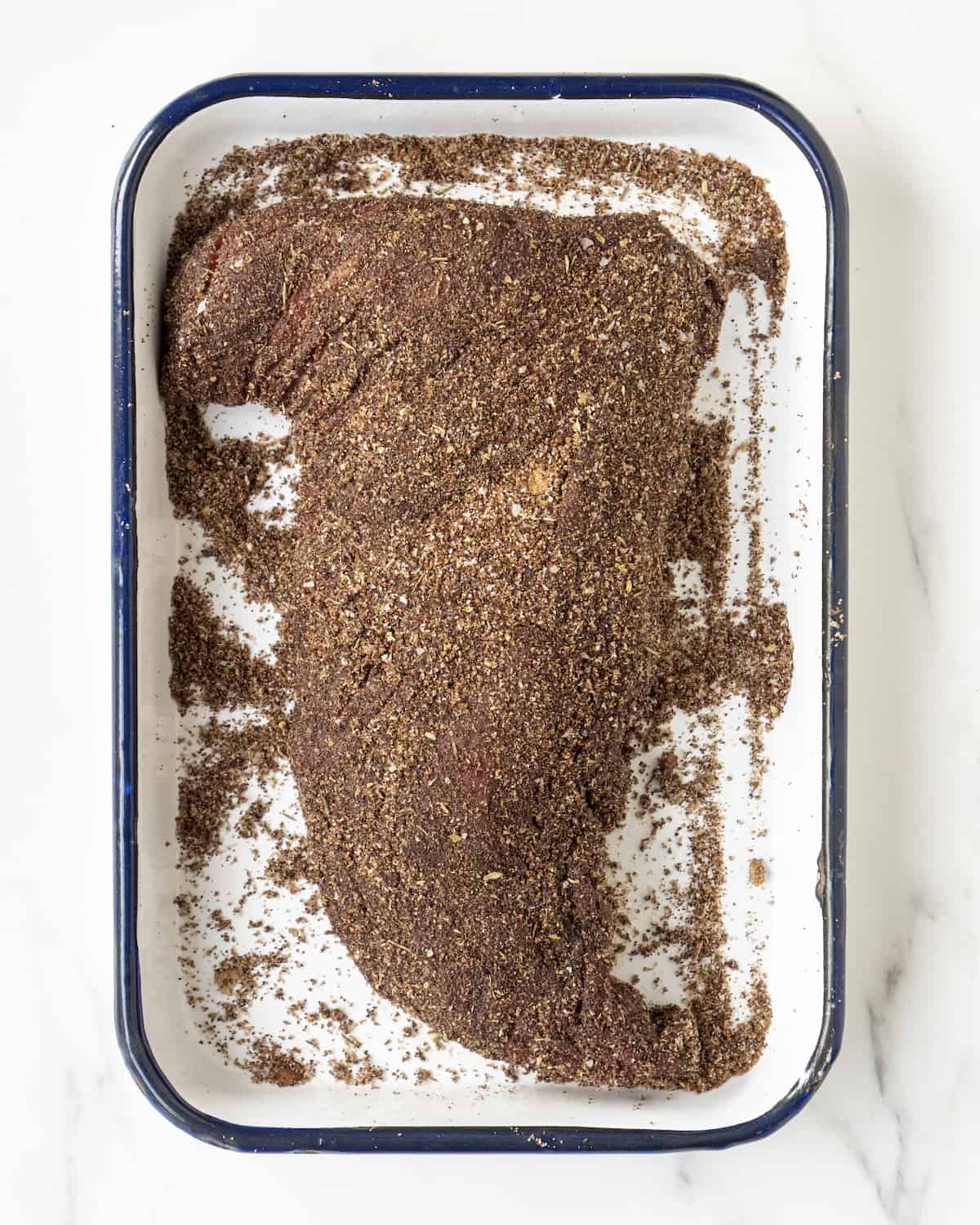 A cut of tri-tip sitting in a baking dish covered with the meat rub.  