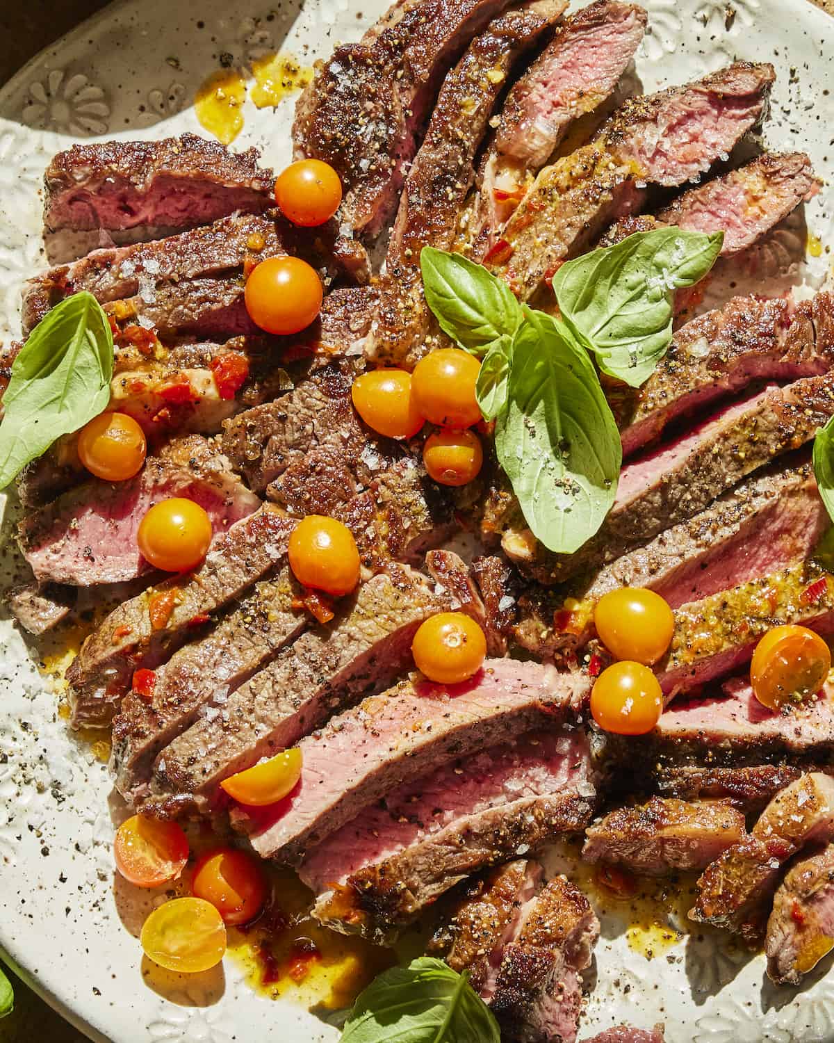 Strips of medium rare ribeye steak with halved cherry tomatoes and basil leaves topped with salt and pepper.  