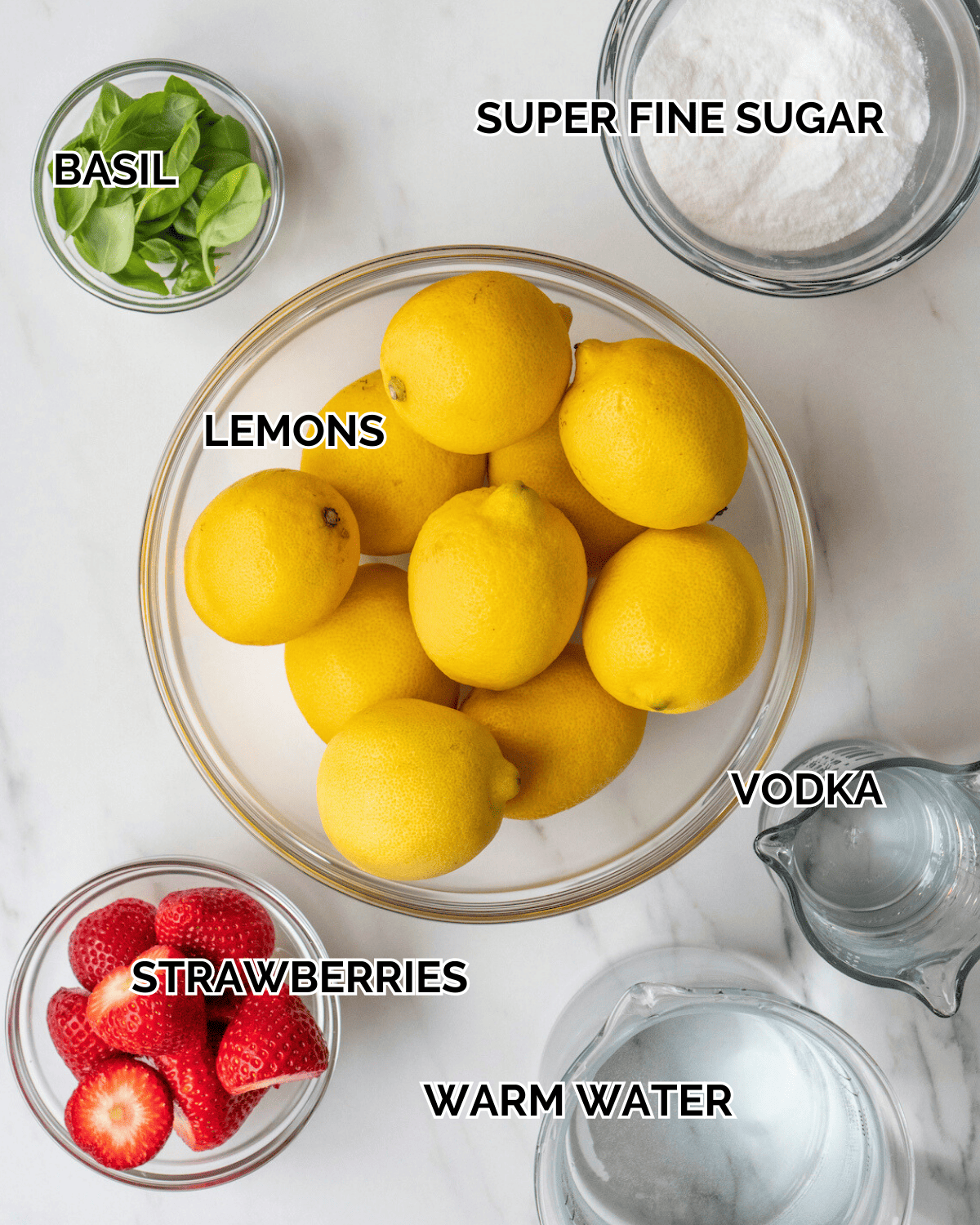 Ingredient shot of ingredients to make strawberry basil lemonade including lemons, vodka, strawberries, warm water, fine sugar, and basil.