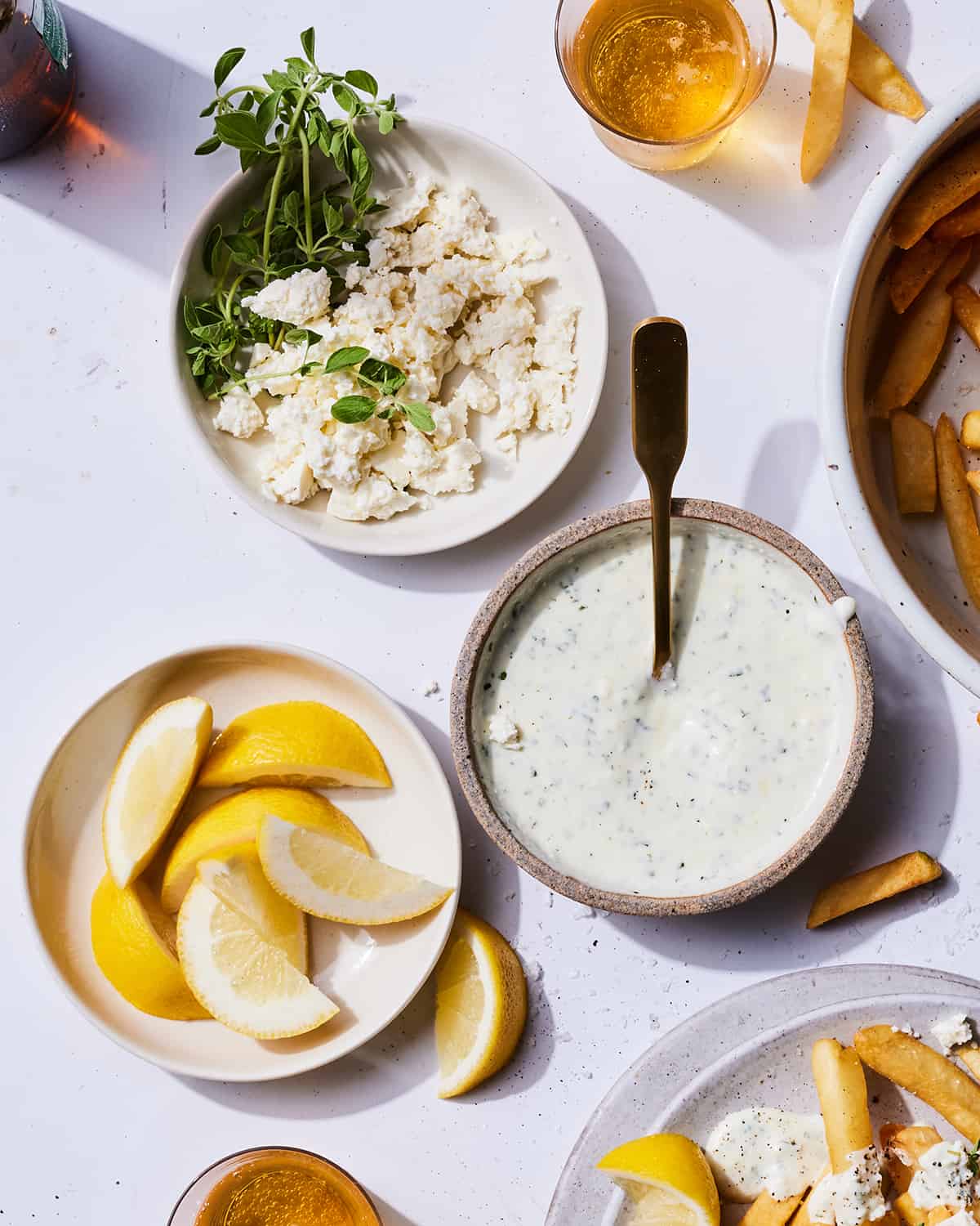 A bowl of feta dipping sauce next to a plate of lemons and a bowl of feta.  
