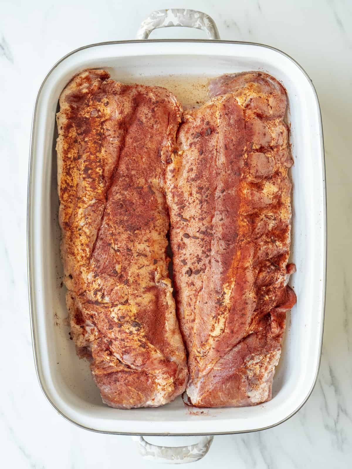 Large baking pan with ribs that have been pat dry and rubbed with chili powder.