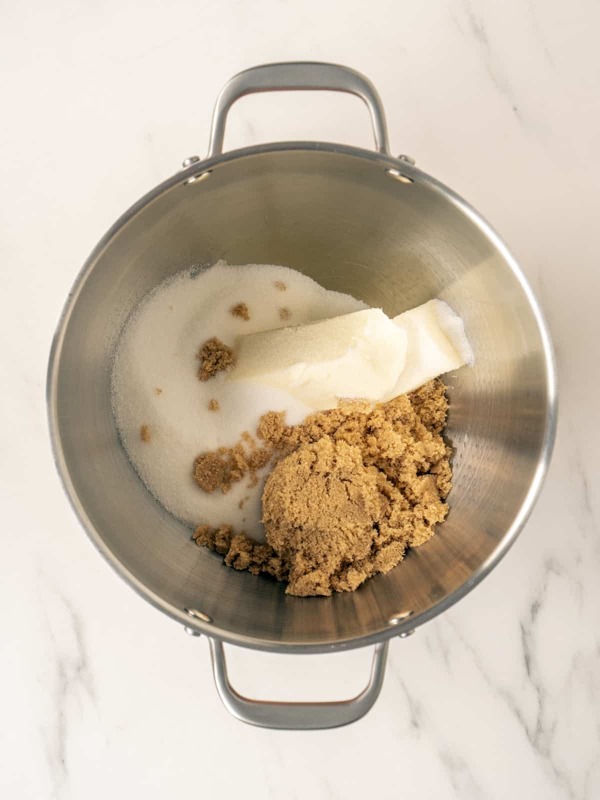 A stand mixer bowl with white sugar, brown sugar and unsalted butter.