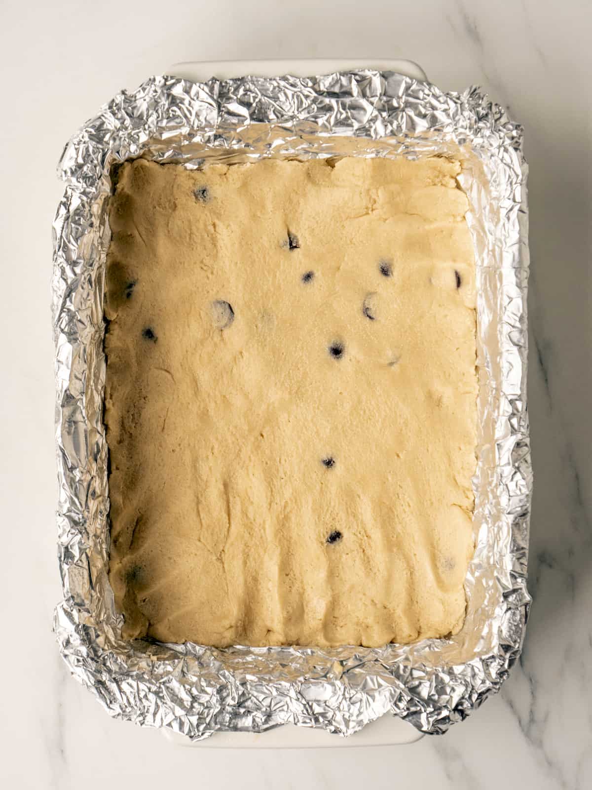 A 9x13 baking pan lined with tin foil with cookie dough pressed into the bottom of the pan into an even layer.