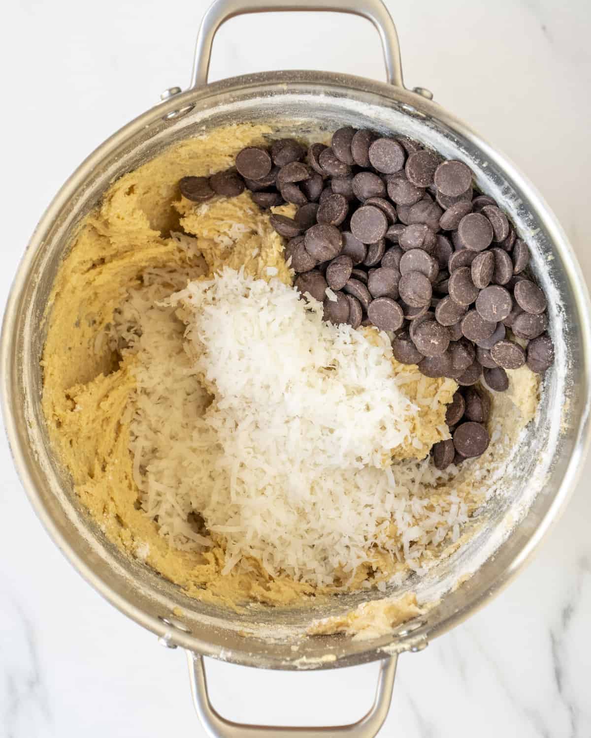 A mixing bowl with cookie dough topped with shredded coconut and chocolate chips.