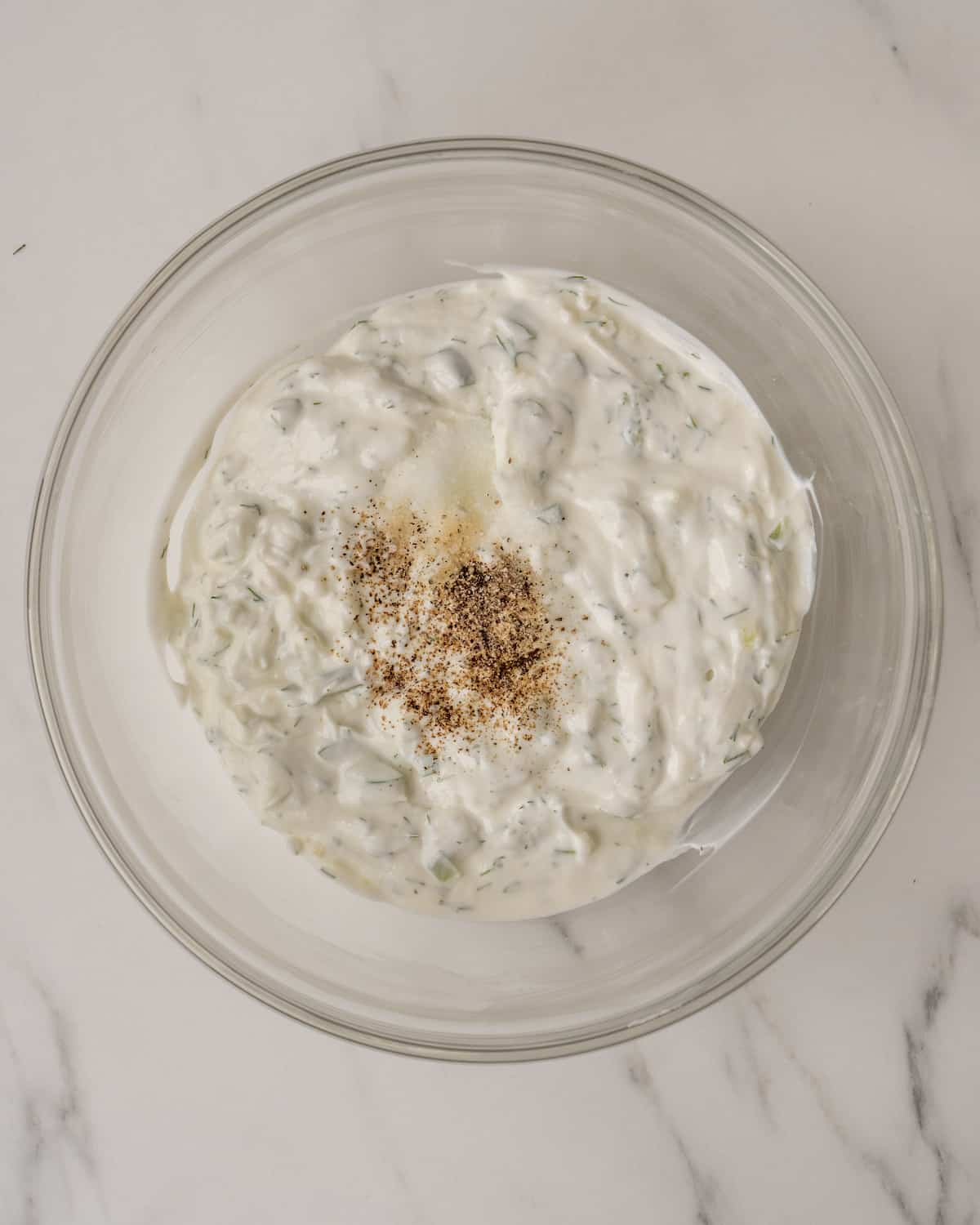 A mixing bowl with tzatziki sauce topped with salt and pepper.