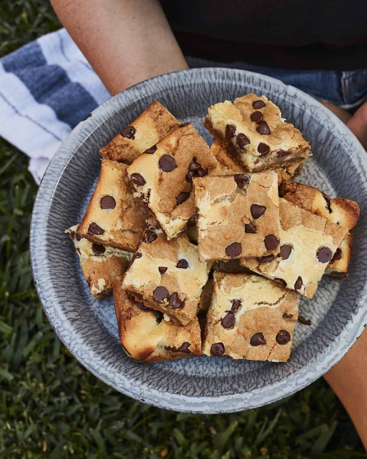A tin of cheesecake cookie bars with chocolate chips being held by a person.  