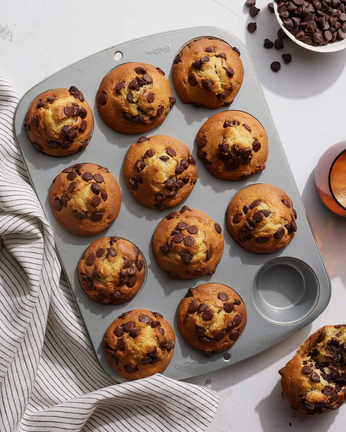 A 3x4 muffin tin with 11 baked muffins. One muffin has been taken out and split in half.  