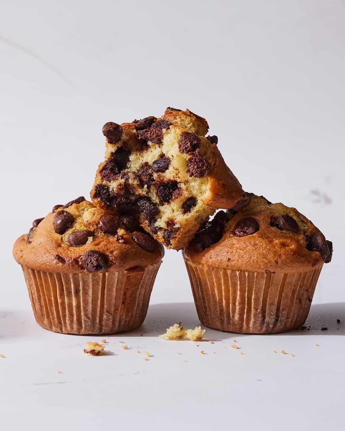 A stack of 3 chocolate chip muffins.  One of the muffins is cut in half to see the inside.  