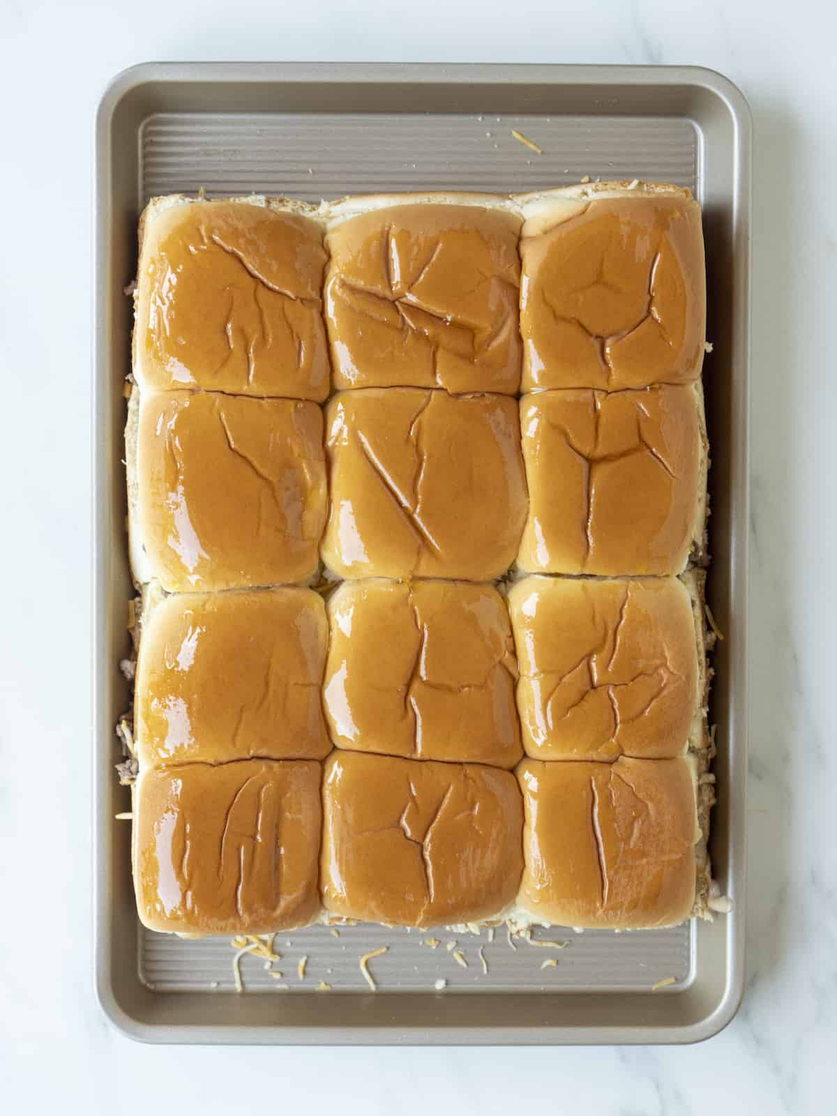 A baking sheet with a 3x4 grid of cheeseburger sliders assembled with all the layers inside.
