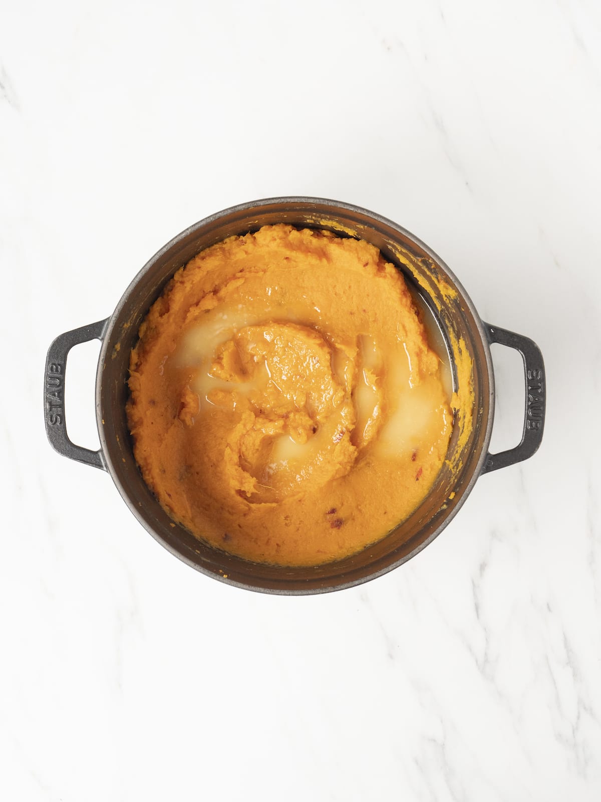 A pot with mashed sweet potatoes and melted butter on top.