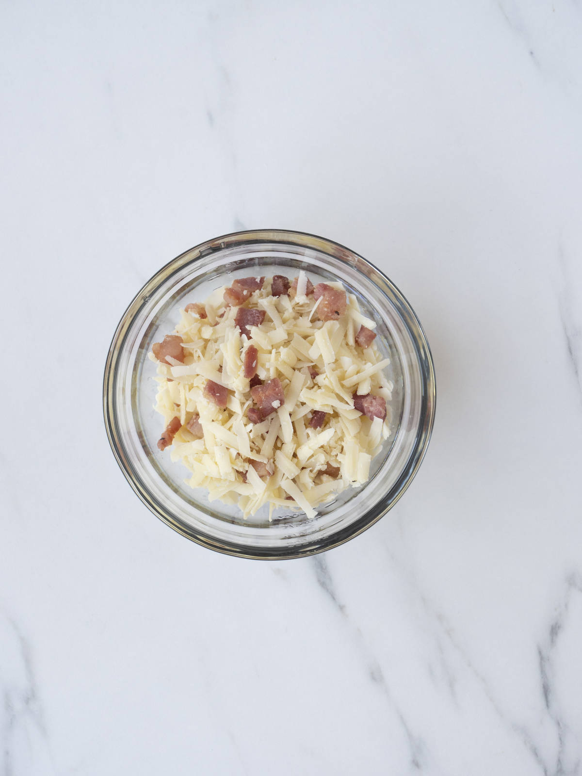 A small glass mixing bowl with a portion of cheese and cooked pancetta mix.