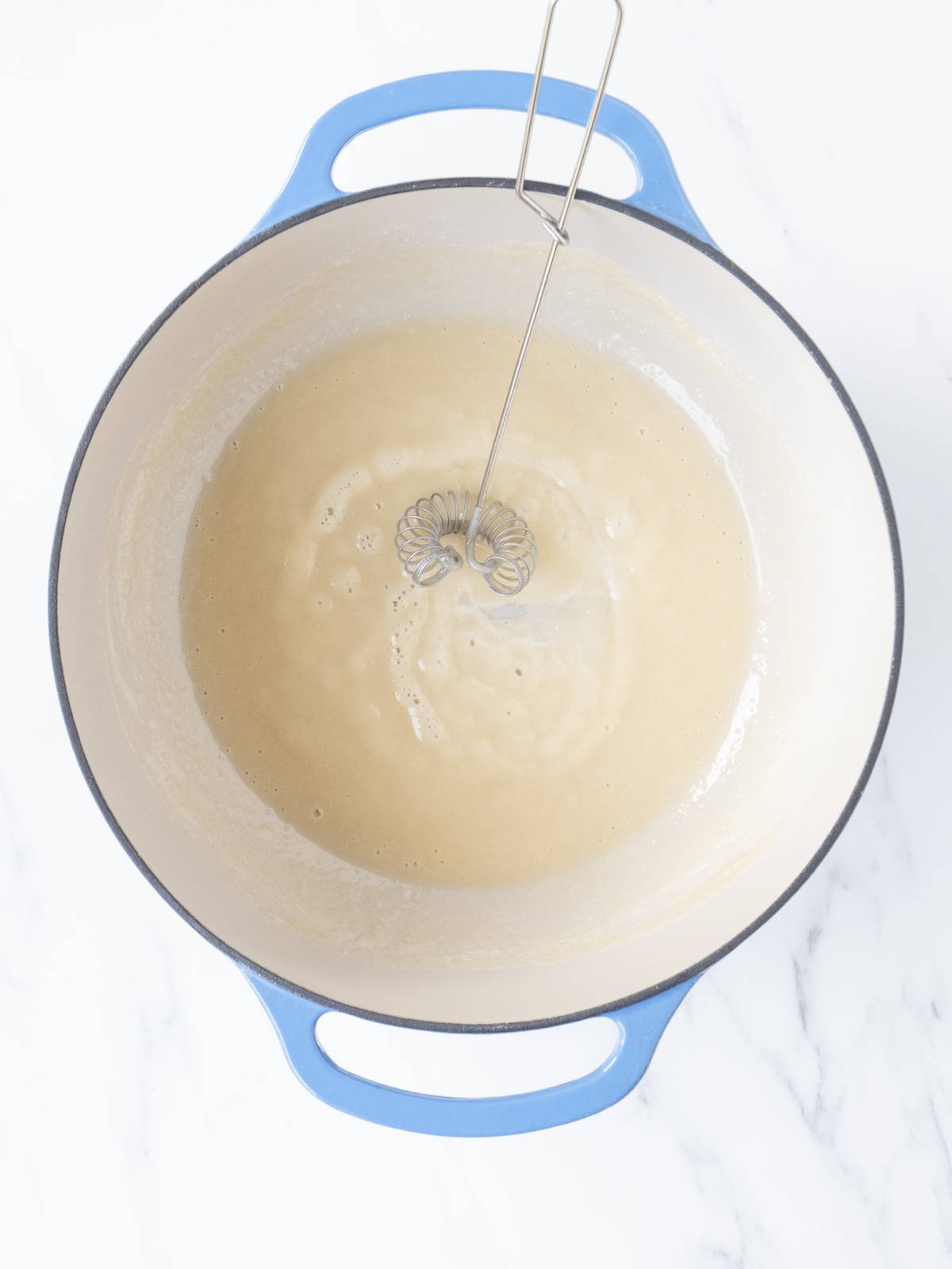 A blue dutch oven with roux made out of butter and flour with a whisk.