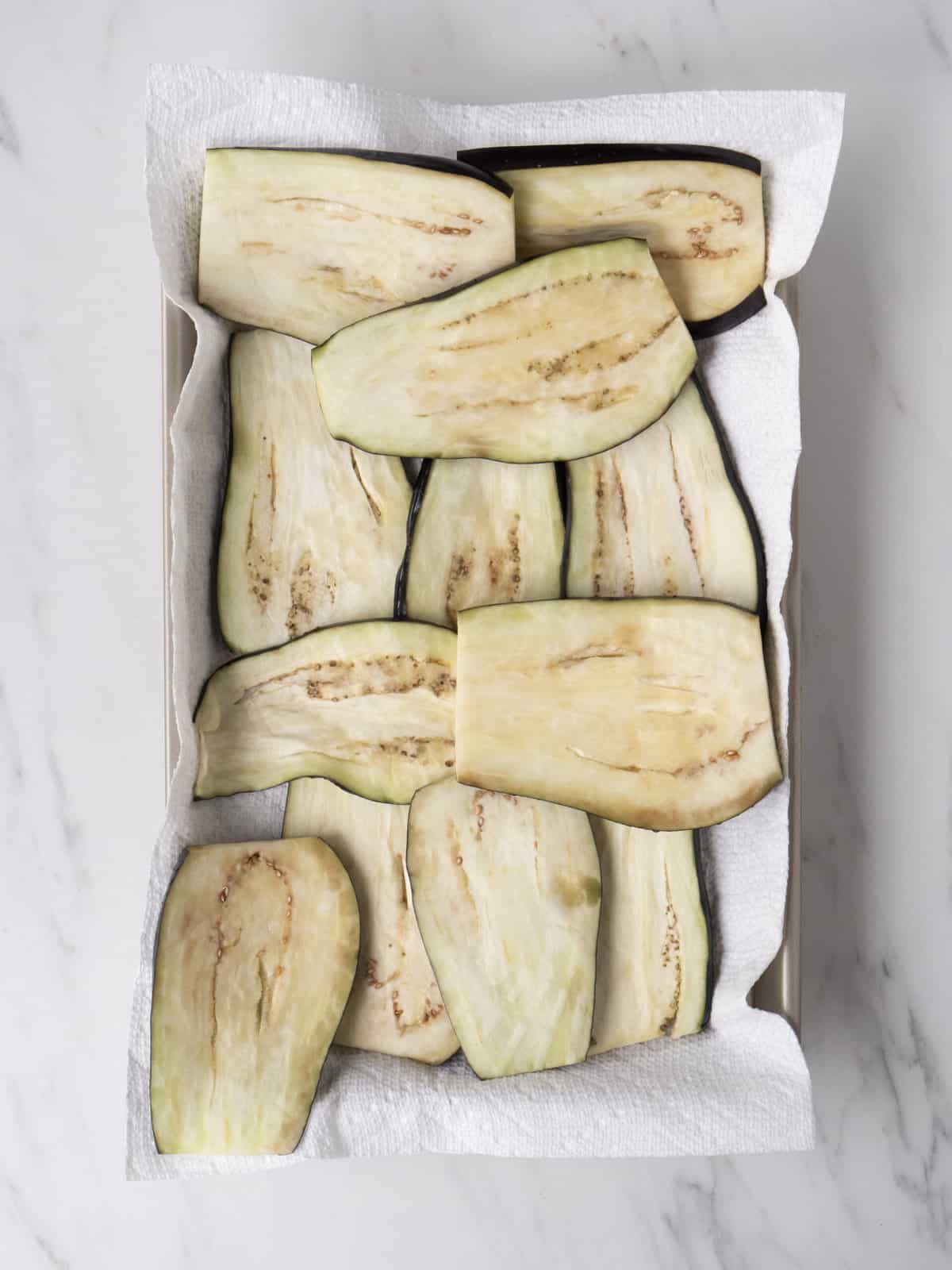 A baking sheet lined with paper towels, with lengthwise cut slices of eggplant topped with salt.
