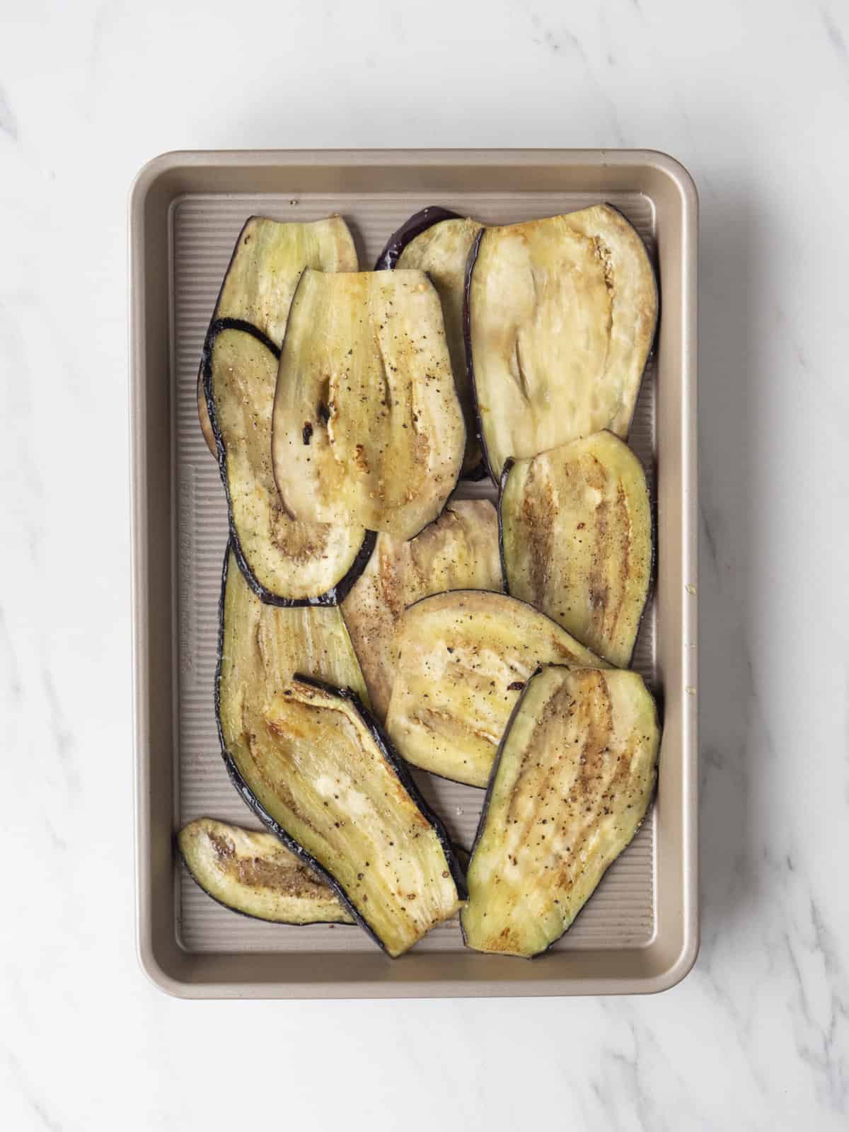A baking sheet with lengthwise cut cooked slices of eggplant.