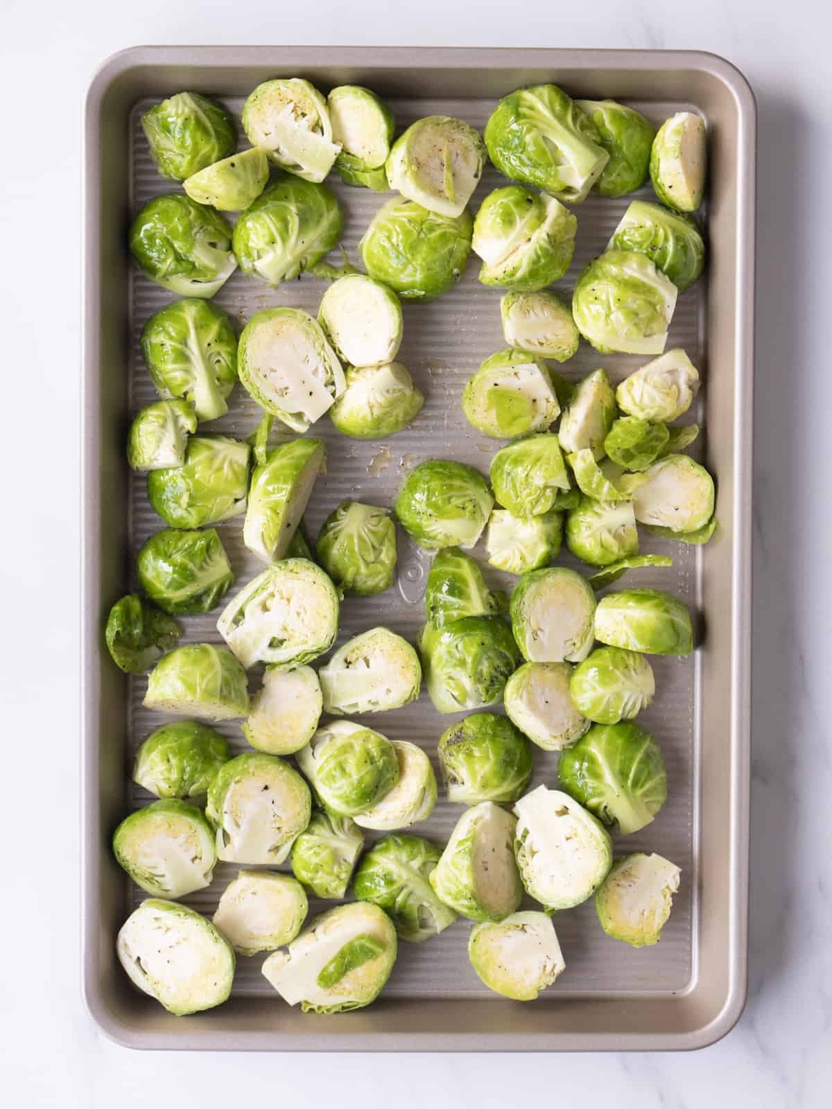 A sheet pan with brussels sprouts spread in a single layer tossed in olive oil.